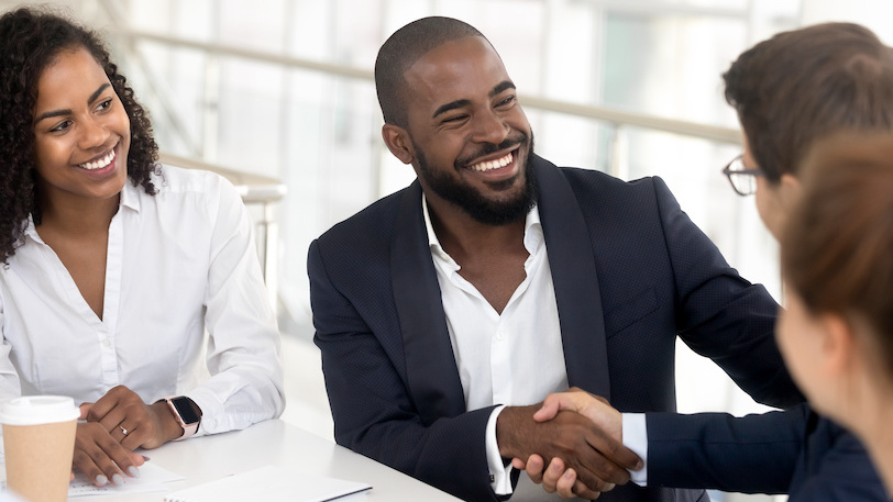 Four business professionals sitting at table shaking hands