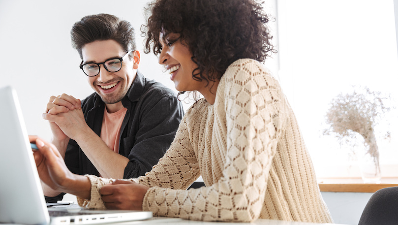 Two young professionals sharing computer and smiling